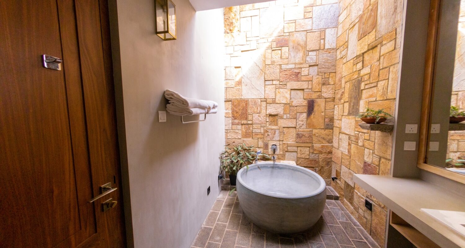 white ceramic bathtub beside brown brick wall
